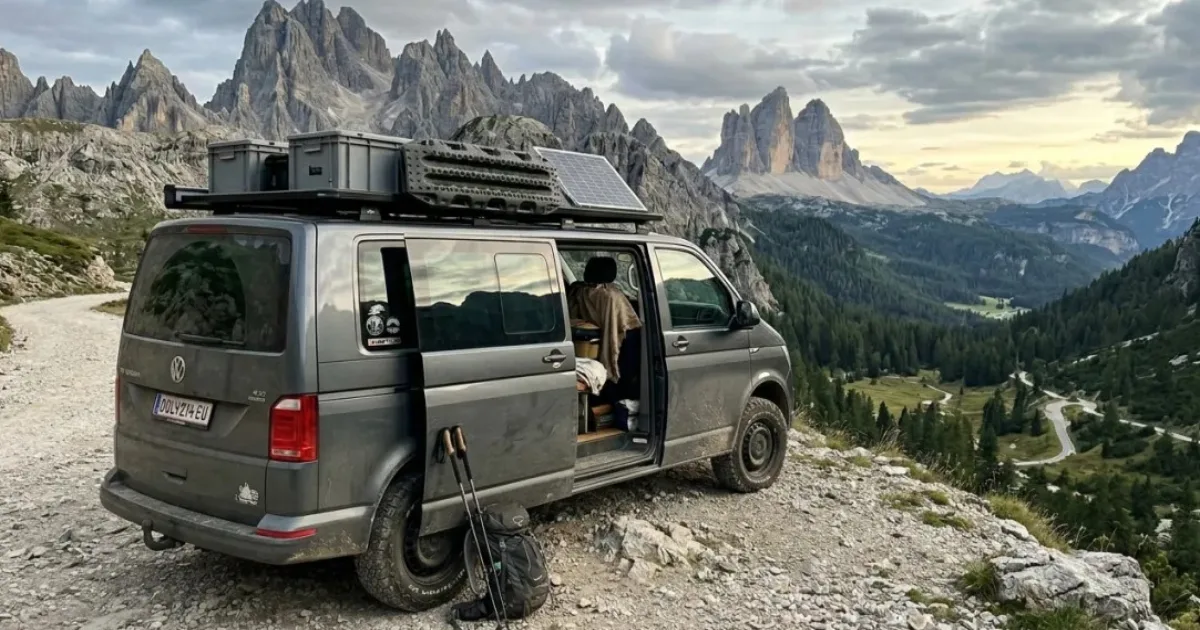 VW Transporter van parked on a gravel mountain road in the Dolomites at sunset, solar panel on the roof